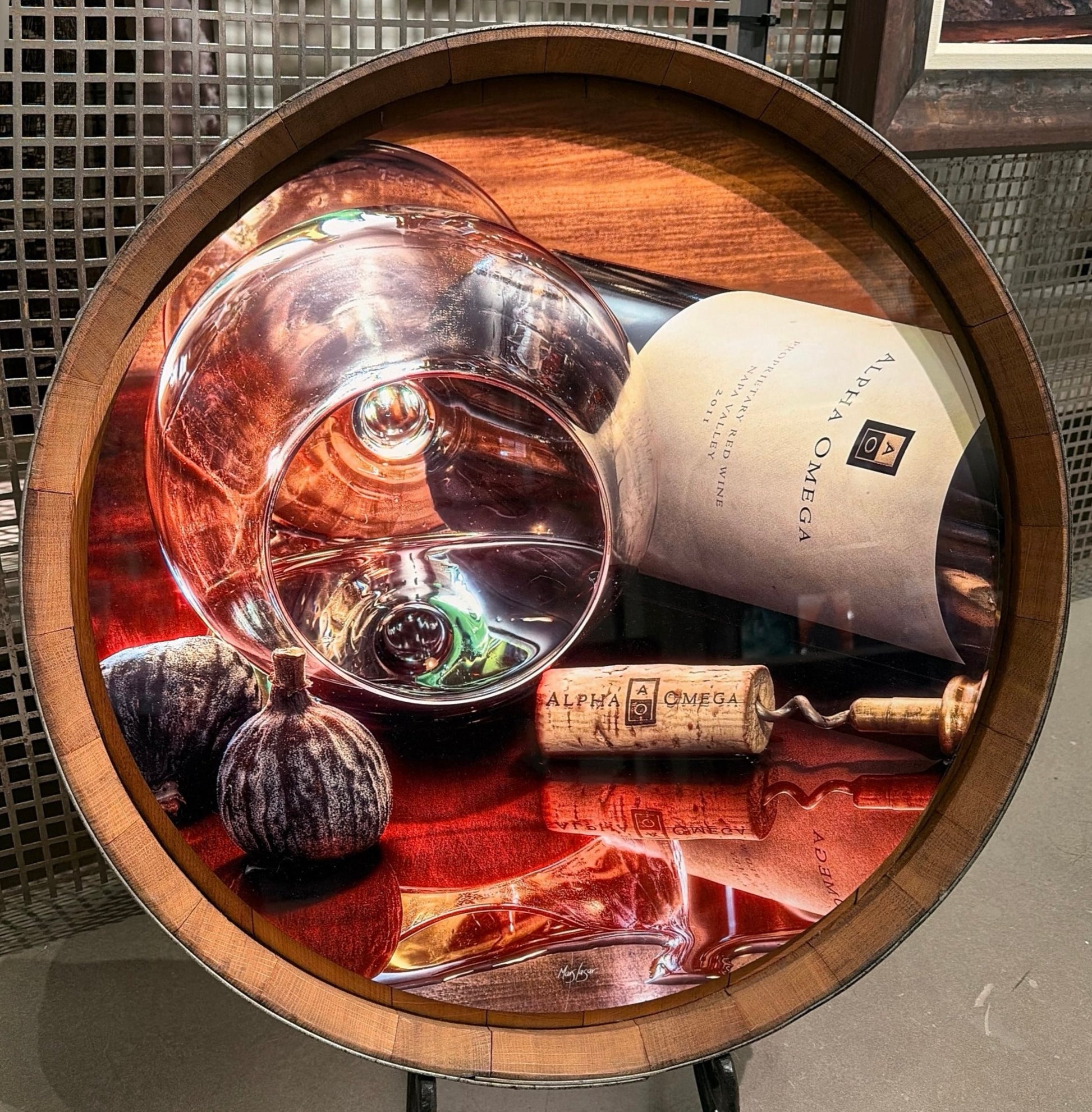 Mars Lasar Alpha Omega Times barrel top artwork featuring a bottle of Alpha Omega wine, wine glass, corkscrew, and cork displayed on an authentic wine barrel top.