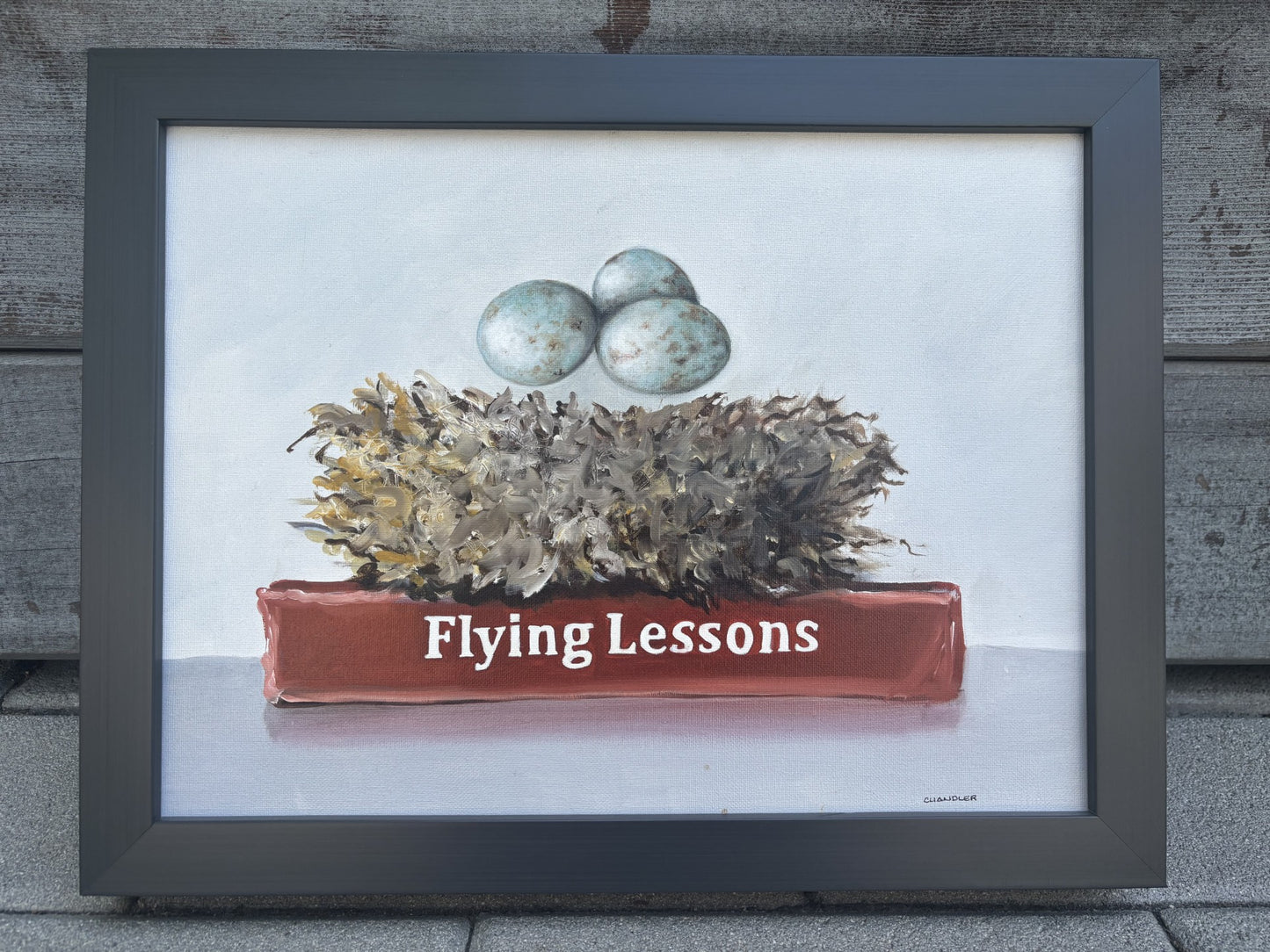 Framed artwork of a nest with flying eggs over a book titled 'Flying Lessons'. Original oil painting on canvas by Gail Chandler.