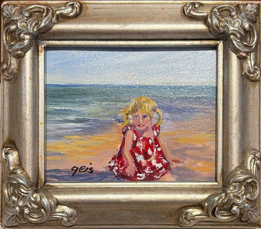 Girl on Beach by Kay Geis, original miniature oil painting of a young blonde girl in a red floral dress sitting on a sandy beach beside the ocean in an ornate silver frame.